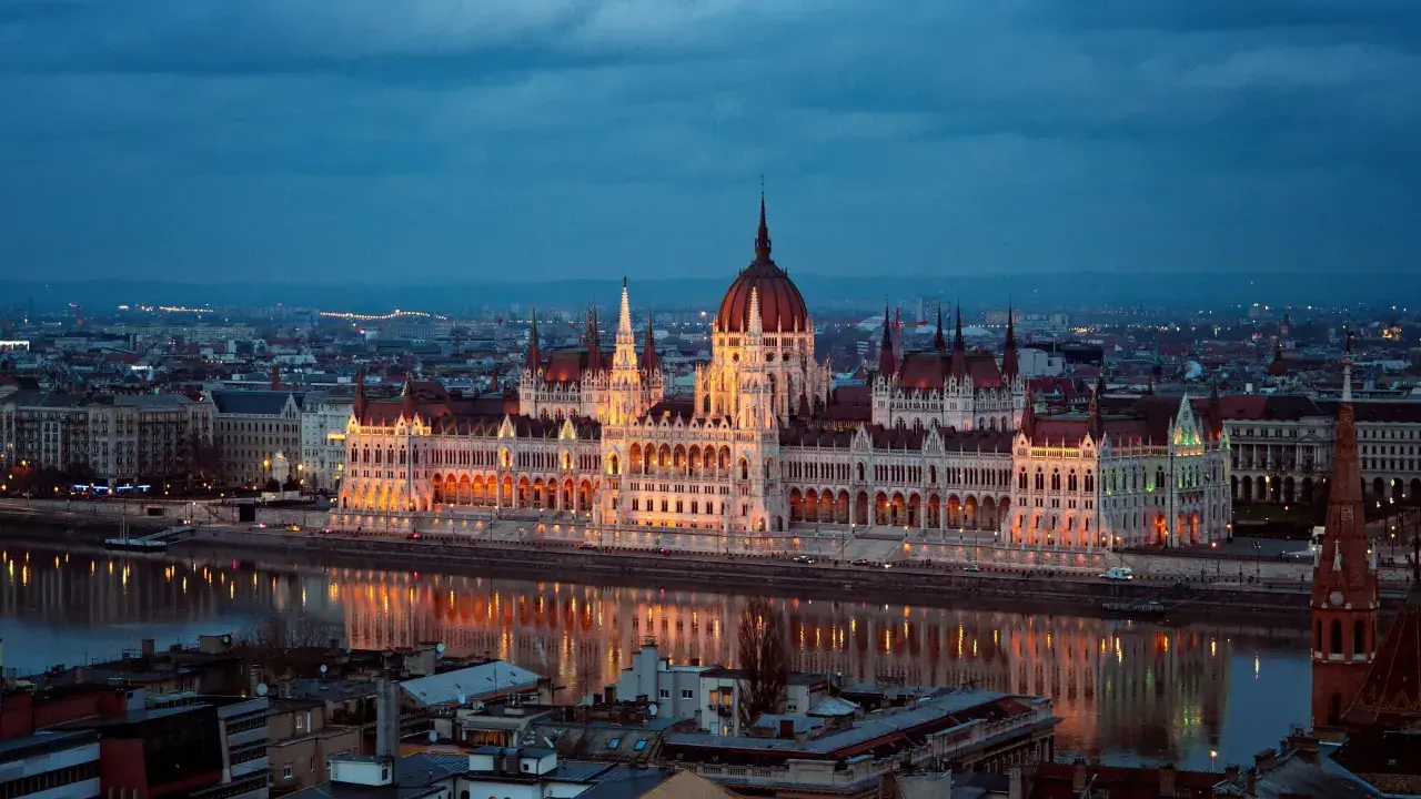 Budynek Parlamentu w Budapeszcie nocą, odbijający się w Dunaju. Miasto tętni życiem, aspirując do miana najbardziej imprezowych miast w Europie.