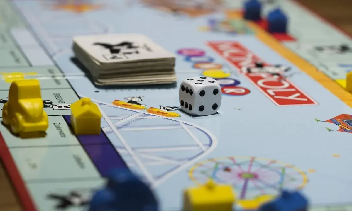 Kostka i pionki na planszy Monopoly. Gra planszowa uczy strategii, negocjacji i zarządzania finansami, realizując cele i zadania.