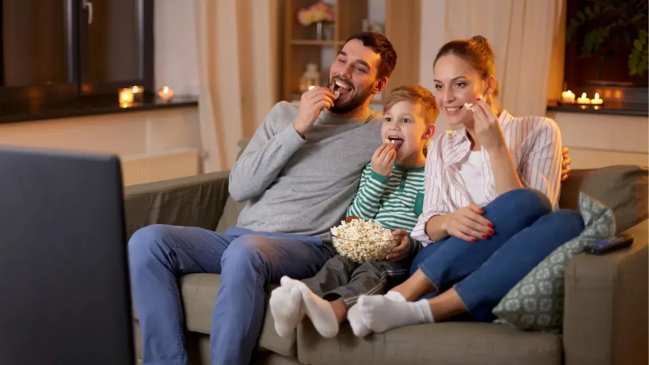 Rodzina śmieje się, jedząc popcorn podczas oglądania wzruszających filmów familijnych.