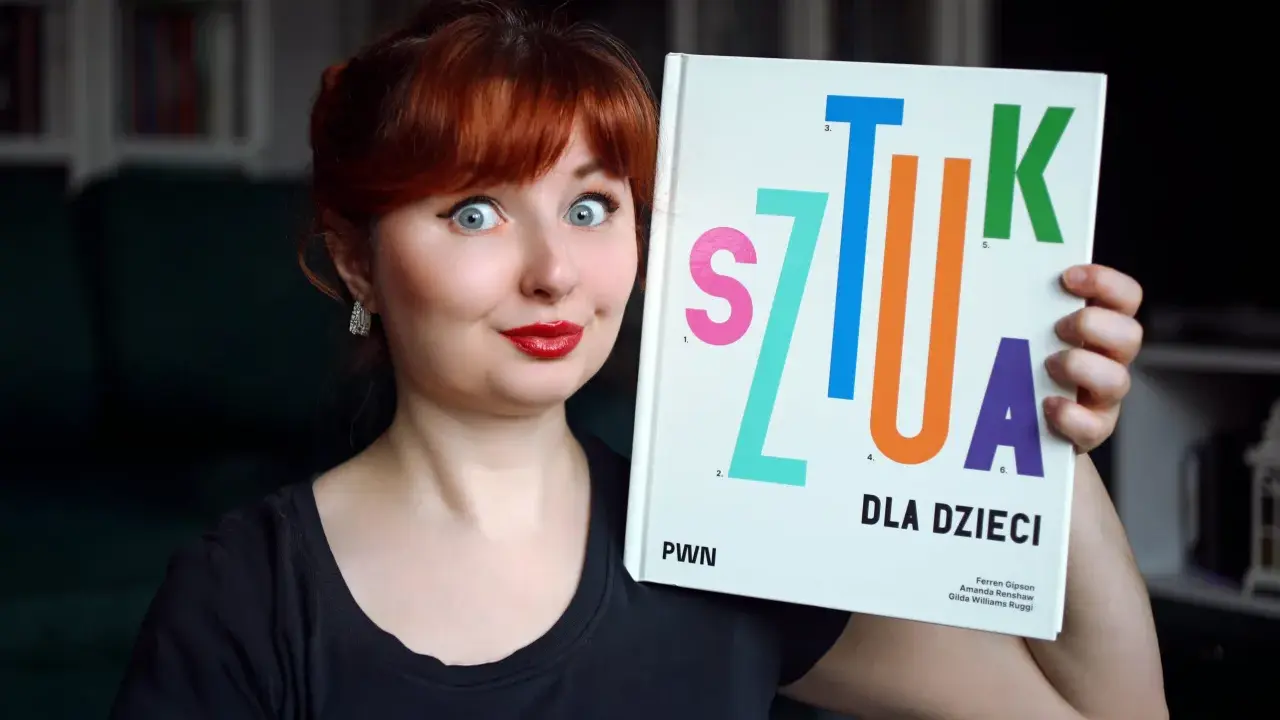 Kobieta z rudymi włosami trzyma książkę "Sztuka dla dzieci". Jej oczy są szeroko otwarte, a usta umalowane na czerwono.