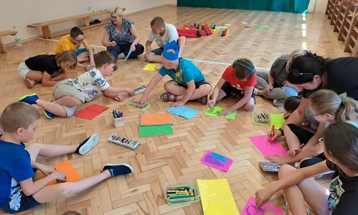 Dzieci biorą udział w zabawach animacyjnych, rysując na kolorowych kartkach.