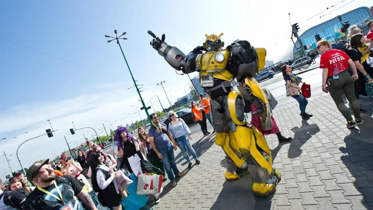 Bumblebee wita fanów na Pyrkonie. Tłum ludzi w kostiumach i z torbami idzie chodnikiem.