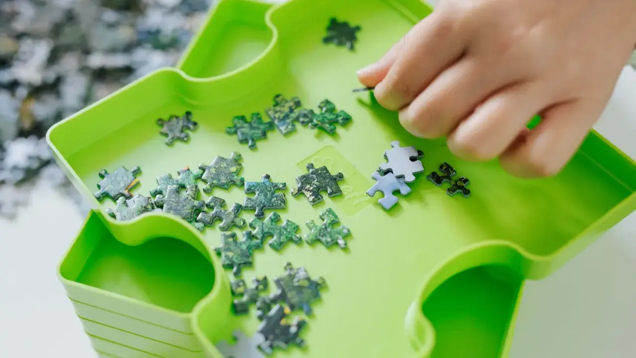 Dłoń układa zielone i niebieskie elementy układanki. To świetna zabawa, by układać puzzle po angielsku.