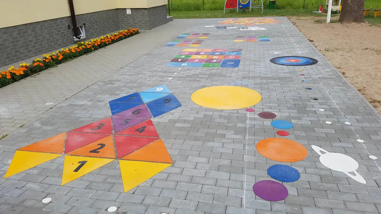 Kolorowe gry plenerowe na placu zabaw: rakieta z liczbami, układ planet i plansza do gry.