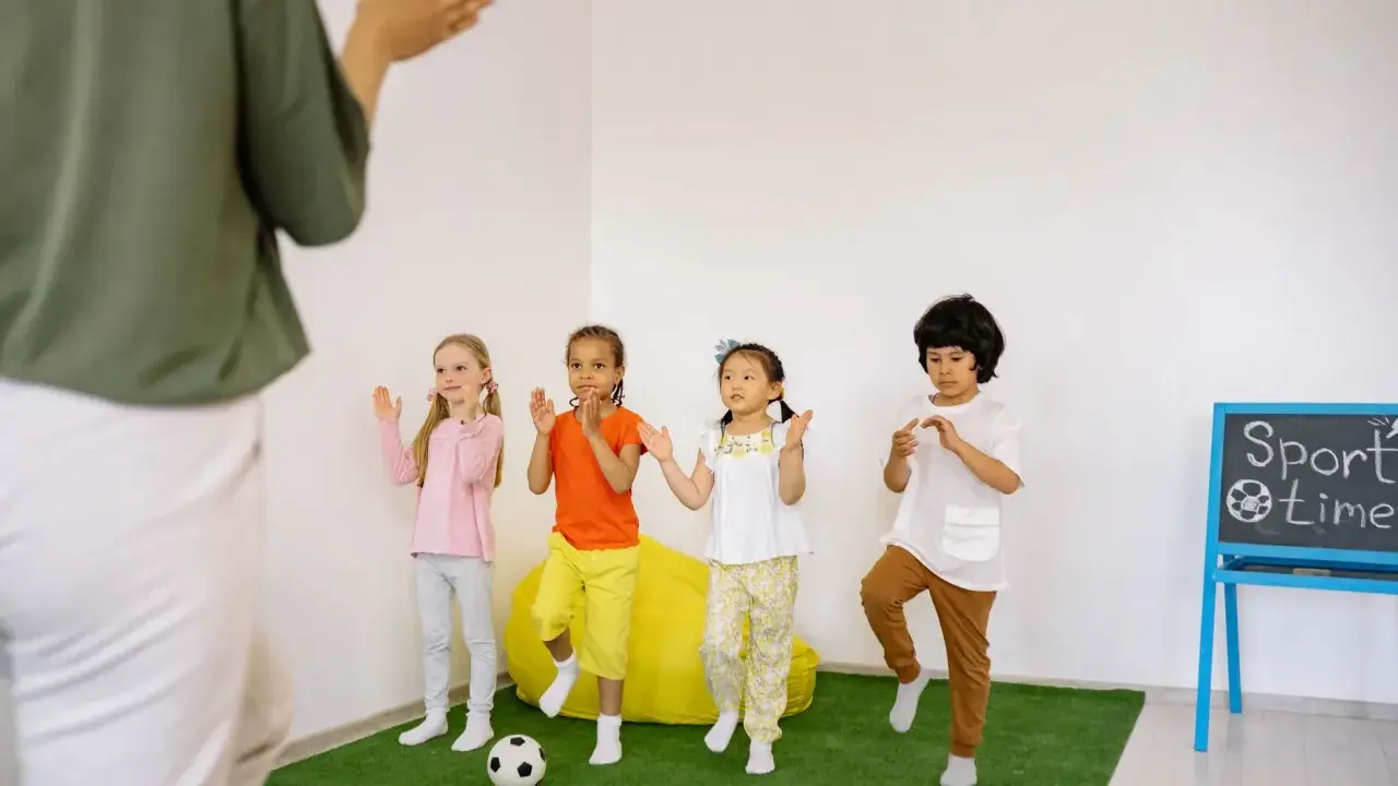Dzieci ćwiczą przy tablicy z napisem "Sport time". Krótkie hasła sportowe dla dzieci motywują do ruchu.