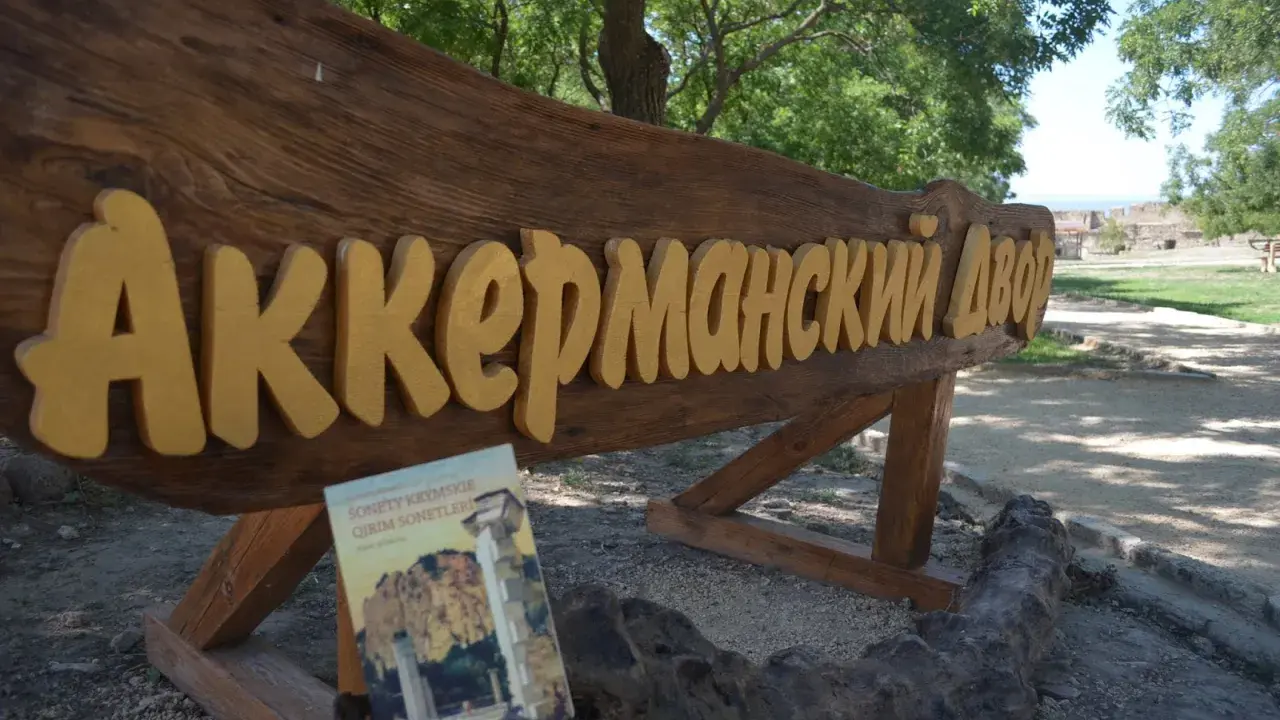 Drewniany napis "Аккерманский Двор" i książka "Sonety Krymskie" na tle stepów akermanskich i ruin.