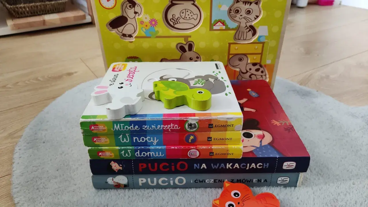 Zabawki dla 1,5 rocznego dziecka: drewniana układanka ze zwierzątkami i stos książeczek "Akademia Mądrego Dziecka" oraz "Pucio".