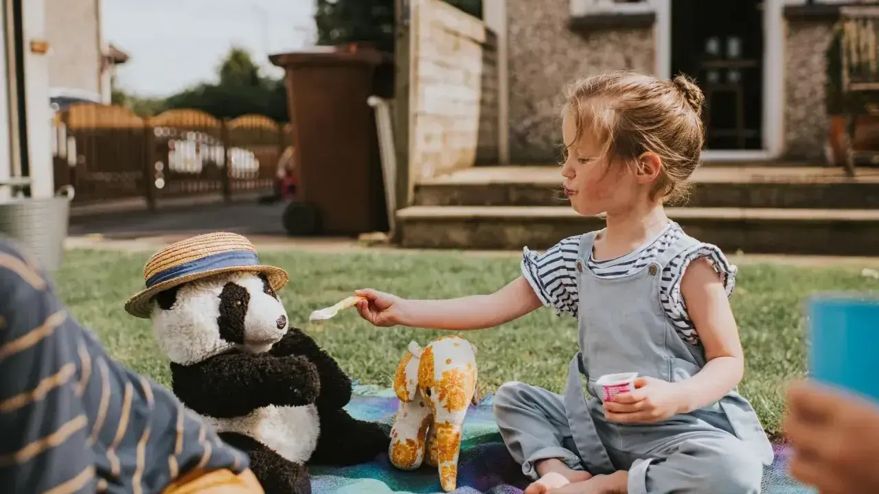 Dziewczynka karmi pluszową pandę na pikniku. Świetny sposób, co robić na nudę w ogrodzie!