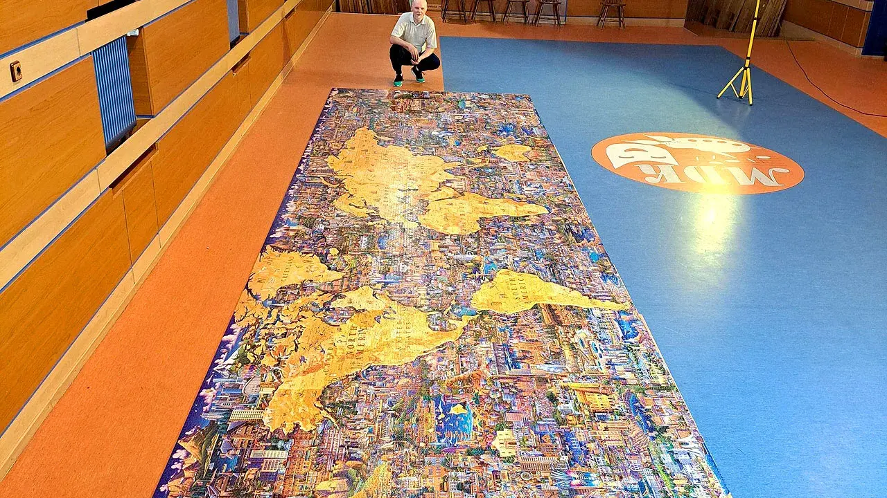 Mężczyzna kuca przy największych puzzlach na świecie, przedstawiających mapę świata z detalami miast.