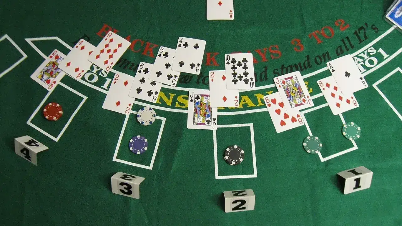 Stół do gry w blackjacka, karty i żetony. Widać karty z numerami i figurami, a także napisy "BLACKJACKS 3 TO 2" i "stand on all 17's".