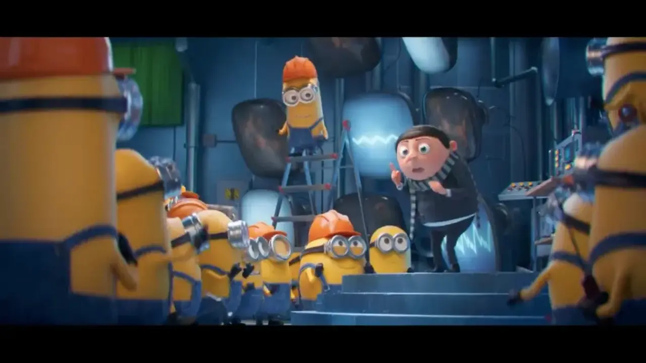 Gru przemawia do grupy minionków, które pracują w laboratorium. Widać różne minionki części, niektóre w kaskach.