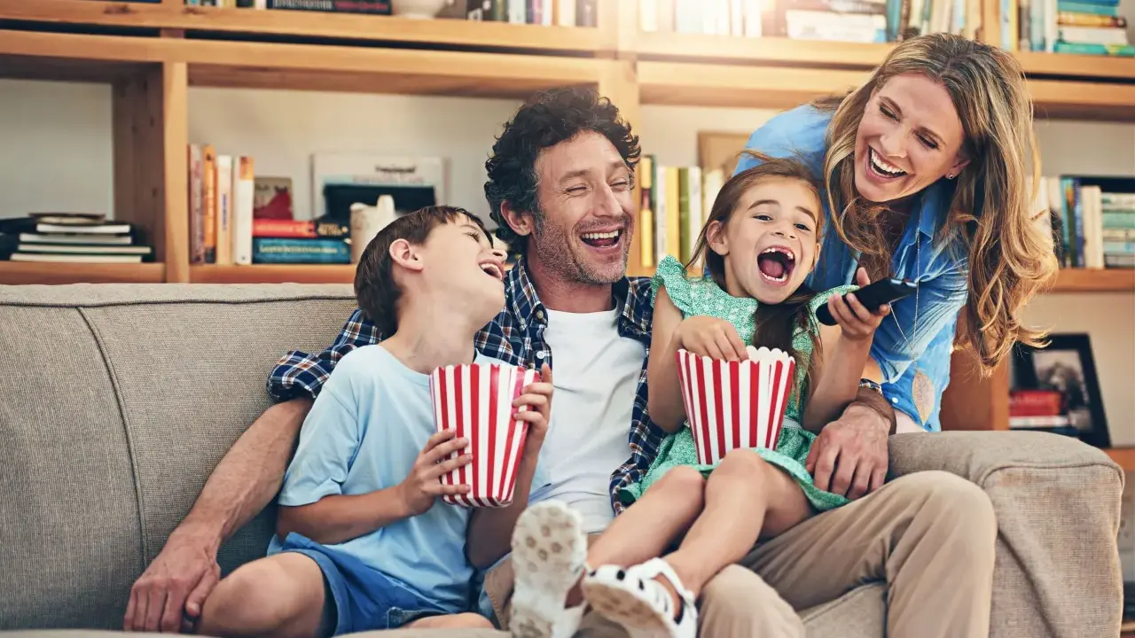 Rodzina śmieje się do rozpuku, jedząc popcorn podczas oglądania filmu dla całej rodziny.