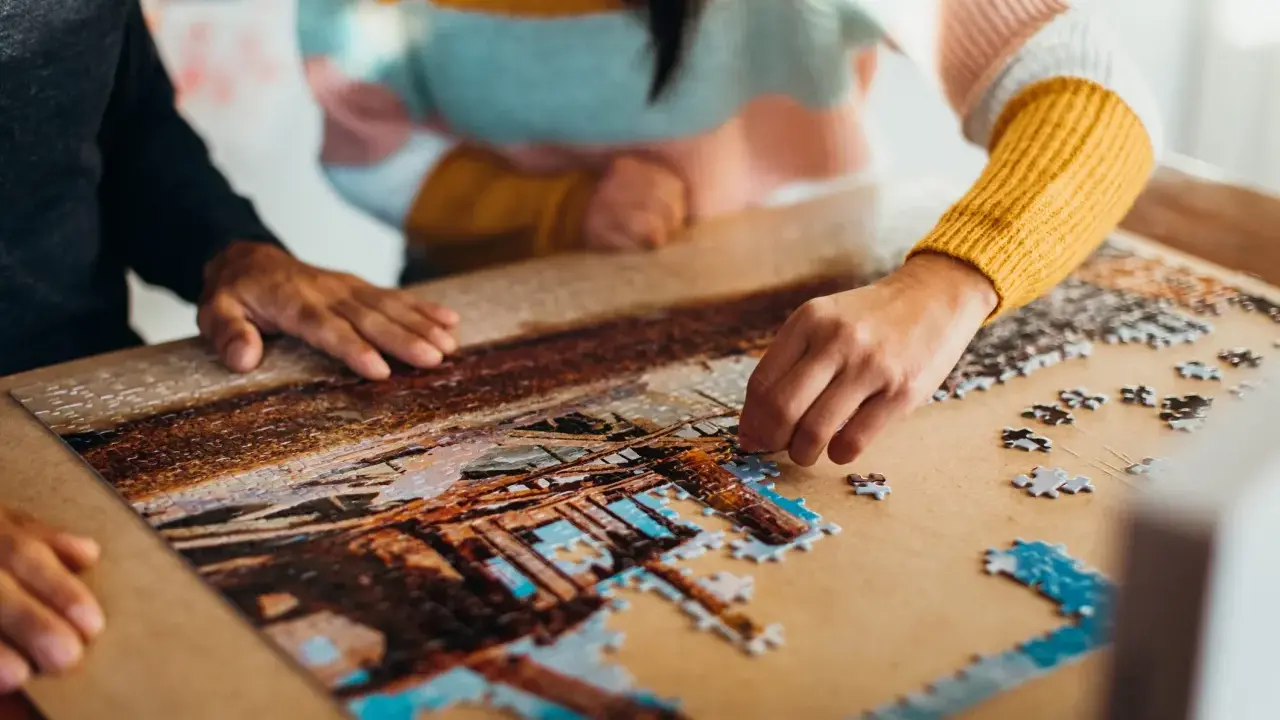 Dwie osoby składają puzzle, tworząc obraz. To dowód na to, że najlepsi producenci puzzli tworzą dzieła, które łączą ludzi.