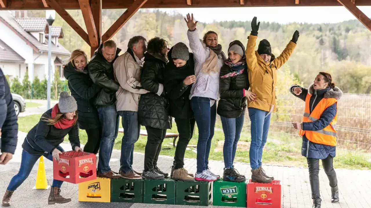 Uczestnicy zabawy, w ramach konkurencji sportowych dla dorosłych, tworzą łańcuch, balansując na skrzynkach po piwie.