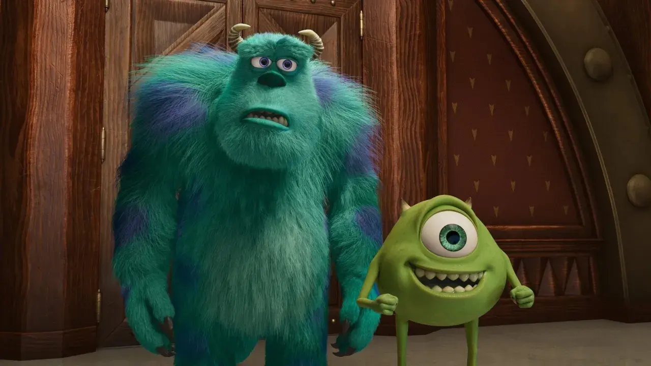 Sully i Mike, bohaterowie bajek z 4 postaciami, stoją obok siebie. Sully wygląda na zmartwionego, a Mike uśmiecha się szeroko.