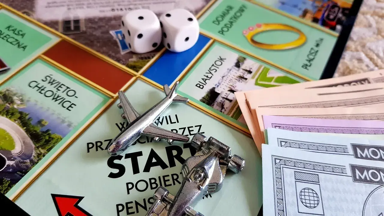 Gra Monopoly, kostki, pionki (samolot, bolid), pieniądze i plansza z polskimi miastami. Różne rodzaje gry wciągają graczy w świat finansów.