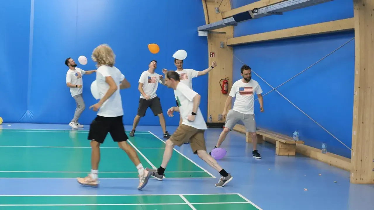 Mężczyźni w koszulkach z amerykańską flagą grają w gry zespołowe dla dorosłych, odbijając balony na hali sportowej.