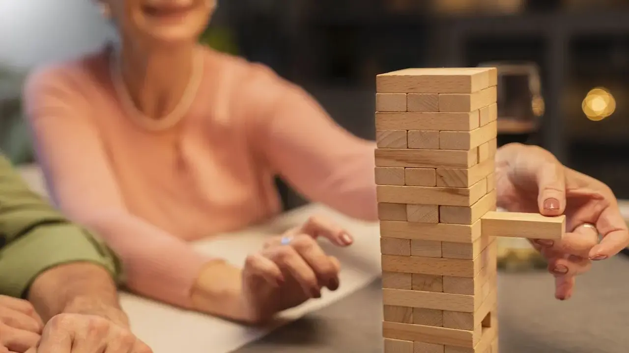 Uśmiechnięta seniorka wyciąga klocek z wieży Jenga. Wspaniałe konkursy zabawy dla seniorów!