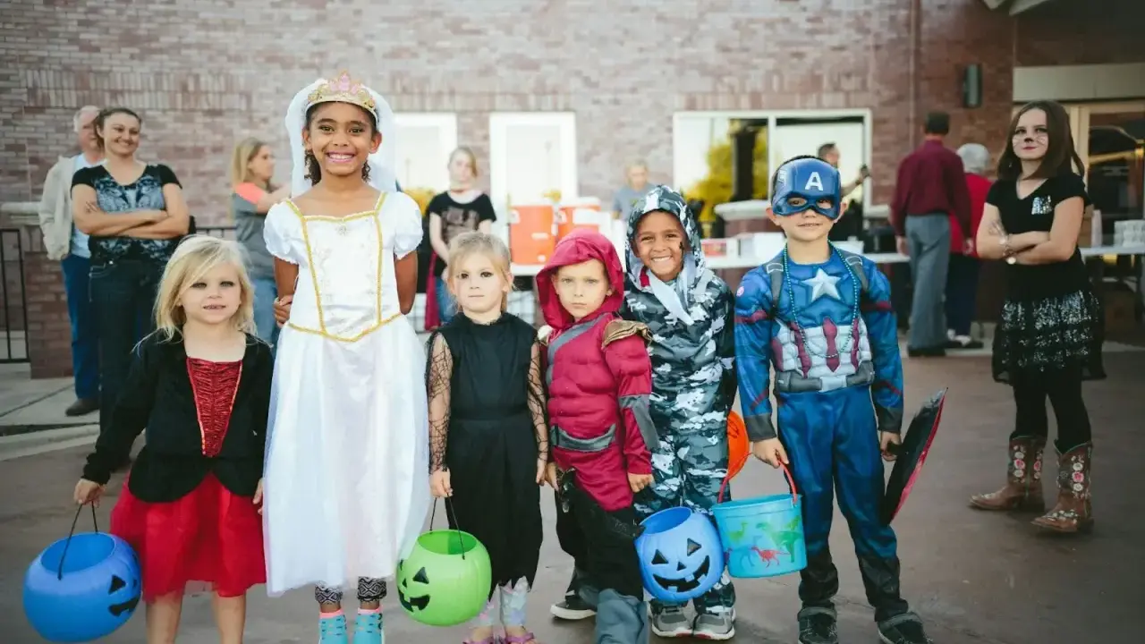 Dzieci w strojach na Halloween, gotowe na psikusy i zbieranie słodyczy. Wśród nich księżniczka, Kapitan Ameryka i inne postacie.