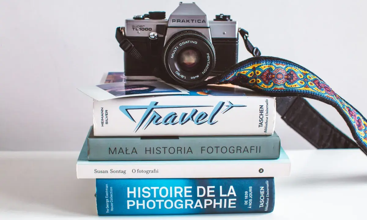 Stos książek o fotografii, w tym "Mała historia fotografii" i "Histoire de la photographie", z aparatem Praktica na górze.