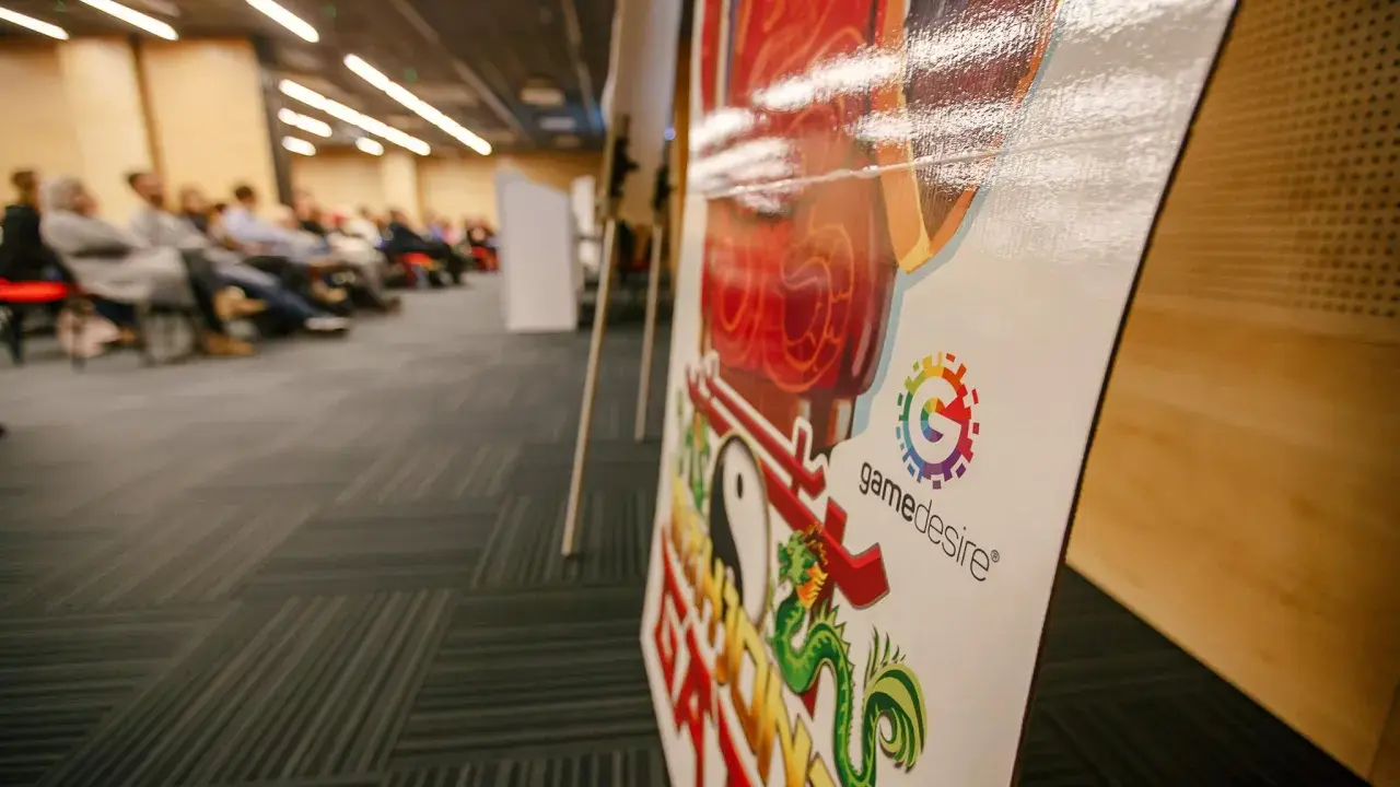 Na konferencji o grach planszowych, z bliska widać planszę z logo "gamedesire" i smoczym motywem.
