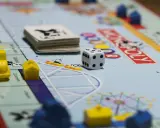 Kostka i pionki na planszy Monopoly. Gra planszowa uczy strategii, negocjacji i zarządzania finansami, realizując cele i zadania.
