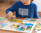 Chłopiec układa kolorowe puzzle ze zwierzątkami. Ukladanie puzzli co ćwiczy? Rozwija spostrzegawczość i zdolności manualne.