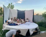 Dzieci siedzą na wielkim materacu pod gołym niebem, oglądając film. To idealne urodziny na dworze z magicznymi światełkami i wygodnymi kocami.