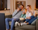 Rodzina śmieje się, jedząc popcorn podczas oglądania wzruszających filmów familijnych.