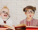 Dzieci w okularach śmieją się i otwierają usta z zaskoczenia, otoczone książkami. Wesołe zabawy w klasie!