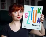 Kobieta z rudymi włosami trzyma książkę "Sztuka dla dzieci". Jej oczy są szeroko otwarte, a usta umalowane na czerwono.
