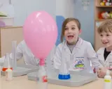 Dzieci w fartuchach laboratoryjnych z ekscytacją obserwują dmuchany balon podczas eksperymentu. To świetna chemia dla dzieci!