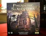 Pudełko gry "Posiadłość Szaleństwa" z mroczną posiadłością i wroną na bramie. Dodatki do tej gry planszowej zapowiadają nowe, przerażające przygody.
