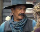 Kevin Costner w filmie z westernowym kapeluszem i chustą na szyi, rozmawia z kobietą.