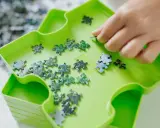 Dłoń układa zielone i niebieskie elementy układanki. To świetna zabawa, by układać puzzle po angielsku.