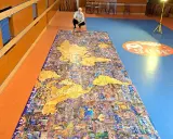 Mężczyzna kuca przy największych puzzlach na świecie, przedstawiających mapę świata z detalami miast.