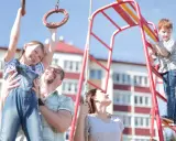 Radosna rodzina na placu zabaw. Ojciec podtrzymuje córkę na kółkach gimnastycznych, syn wspina się po drabince. Zabawy na placu zabaw cele to radość i wspólne chwile.
