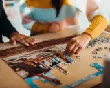 Dwie osoby składają puzzle, tworząc obraz. To dowód na to, że najlepsi producenci puzzli tworzą dzieła, które łączą ludzi.