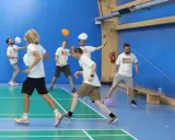 Mężczyźni w koszulkach z amerykańską flagą grają w gry zespołowe dla dorosłych, odbijając balony na hali sportowej.