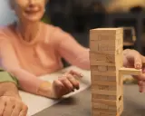 Uśmiechnięta seniorka wyciąga klocek z wieży Jenga. Wspaniałe konkursy zabawy dla seniorów!