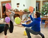 Para i dzieci bawią się balonami, wykonując twórcze zabawy ruchowe przy choince.