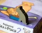 Szary kotek na pudełku gry planszowej "Najlepsza gra o psach". Czas na wspólną grę z pieskami!