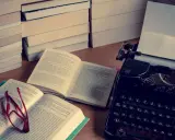 Stos książek, otwarta księga z okularami i zabytkowa maszyna do pisania. Idealne miejsce do tworzenia streszczeń i pisania.