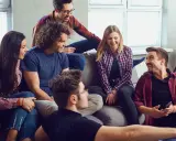 Grupa przyjaciół śmieje się, siedząc na kanapie. Wyglądają, jakby grali w grę, może nawet w Familiadę, odpowiadając na zabawne pytania.