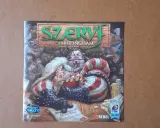 Szeryf z Nottingham gra. Krągły, rubaszny szeryf w bogatym stroju siedzi na drewnianym stole, otoczony ludźmi i monetami.