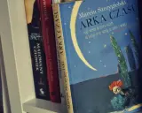 Książka "Arka Czasu" Marcina Szczygielskiego na półce. Ilustracja przedstawia nocne niebo z księżycem i biegnącą postacią.