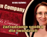 Kobieta z rudymi włosami i okularami uśmiecha się obok planszy gry "John Company". Zarządzanie spółką dla twardzieli.
