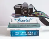 Stos książek o fotografii, w tym "Mała historia fotografii" i "Histoire de la photographie", z aparatem Praktica na górze.