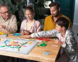 Rodzina gra w planszówkę, ciesząc się wspólnym czasem. To świetny przykład na zalety gier planszowych: rozwijają logiczne myślenie i budują więzi.