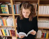 Dziewczynka z warkoczykami czyta książkę na tle regałów pełnych literatury. Może to być streszczenie "Skarbczyka" lub innej lektury.
